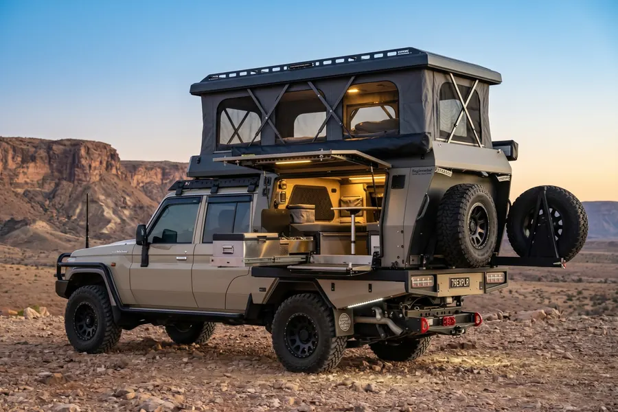 Land Cruiser 79 camper with the hatch open and warm lights on, parked in a rocky desert at dusk